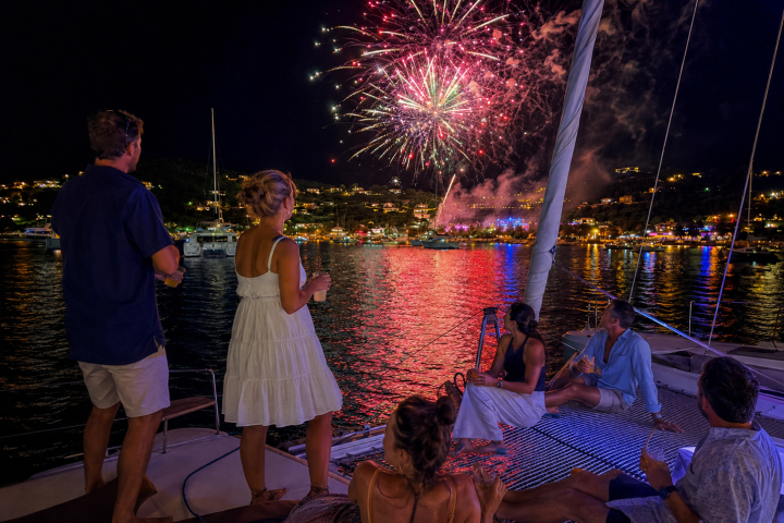 People on a boat watching fireworks over a city at night.