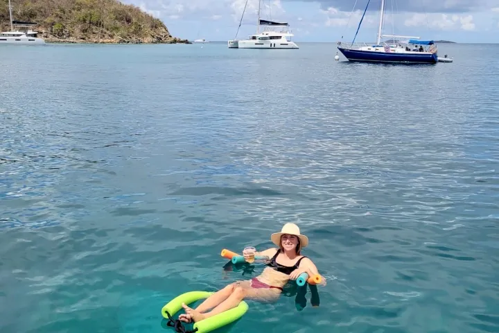 Seas the Day Charters guest holding a drink floating on styrofoam noodles in the Caribbean waters