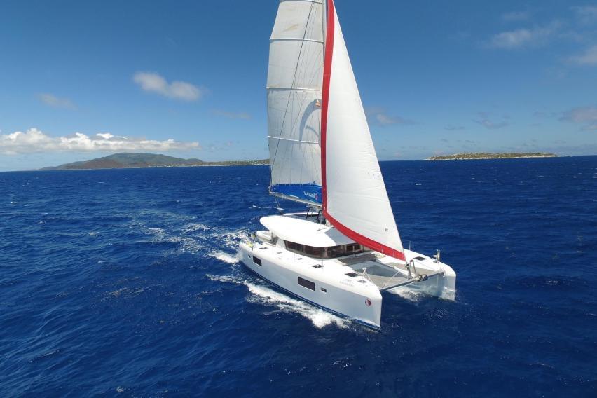 Sailboat cruising on blue ocean with distant islands under clear sky.