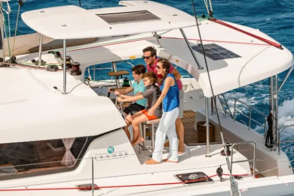 Family steering a catamaran on the ocean with blue waves visible in the background.