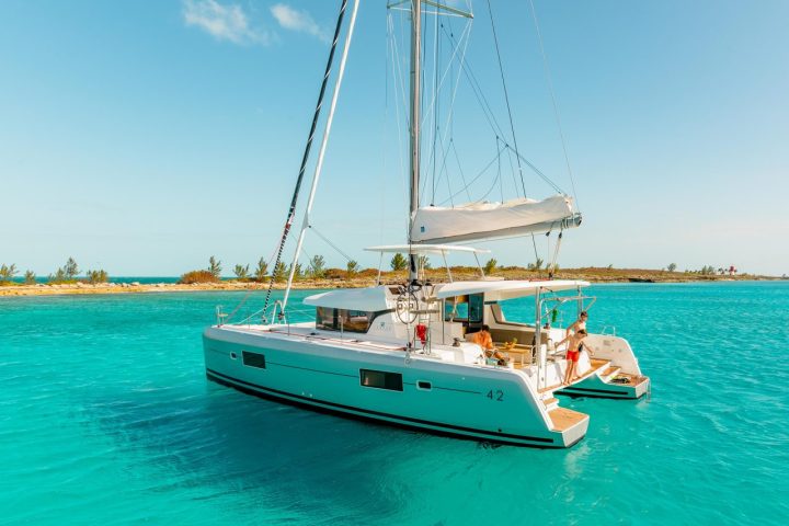Sailboat with people on board in clear blue water near a small island.