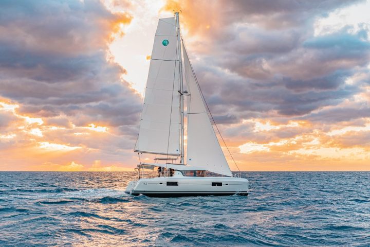 Sailboat on ocean at sunset with dramatic clouds and orange sky.
