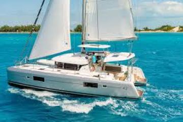 Catamaran with raised sails sailing on turquoise water near a tropical island.