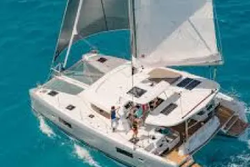 Sailing catamaran gliding on clear blue water with people on deck.