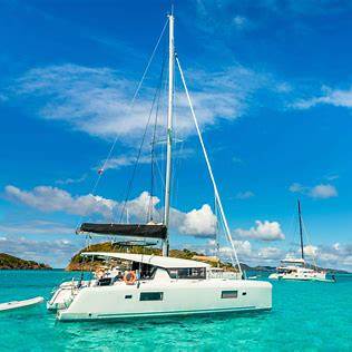 Sailboats anchored in clear turquoise water under a blue sky with clouds.