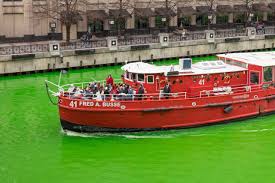 Red boat on bright green river with people on deck.
