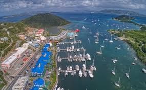 Aerial view of harbor with boats, buildings, and green hills under a cloudy sky.